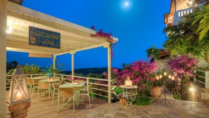 Un patio al aire libre con mesas y sillas, un letrero de Konstantina Studios y flores rosadas floreciendo.