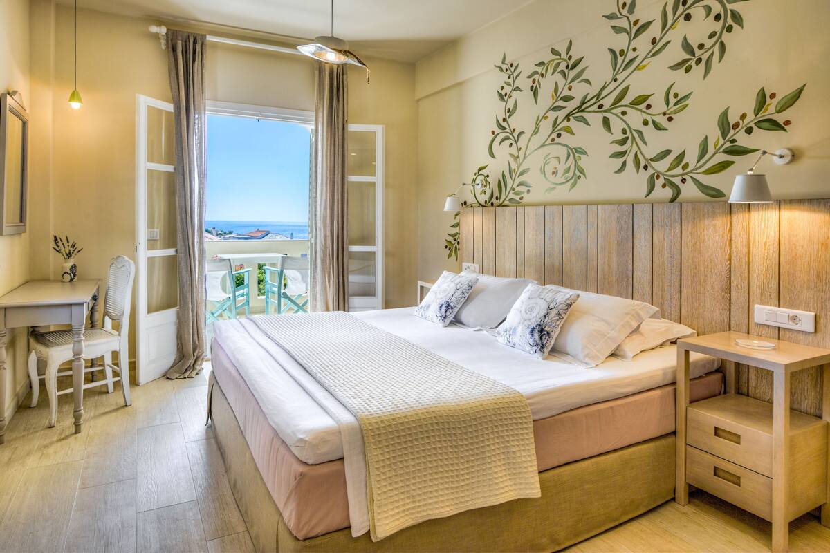 A bedroom with a bed, bedside table, chair, and a view of the sea.
