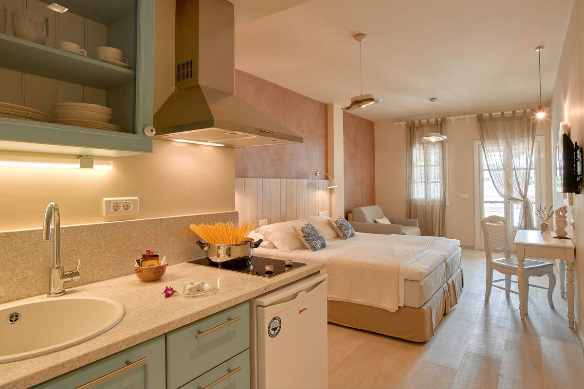 A modern kitchen with a sink, stove, and cabinets, a dining area with a table and chairs, and a bedroom with a bed and curtains.
