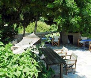 An outdoor seating area with a wooden table and chairs, surrounded by lush greenery and trees. - Konstantina Studios (Alonissos)