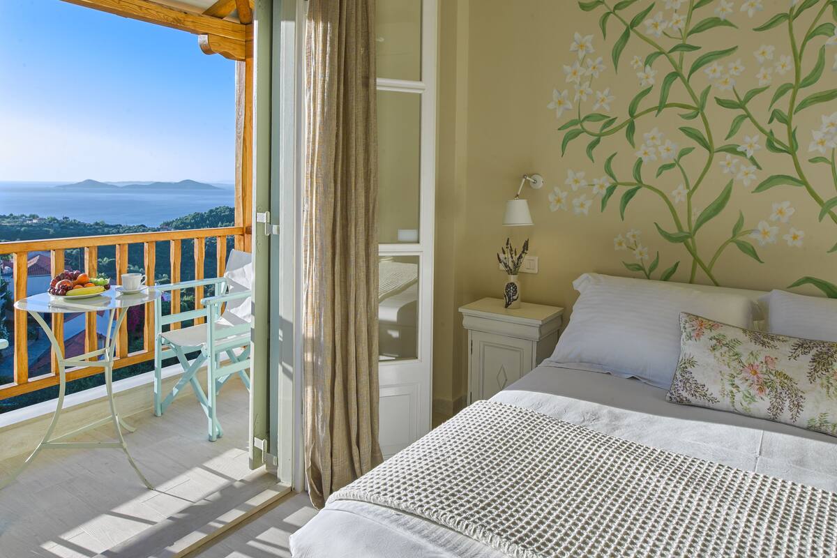 A bedroom with a balcony, a bed with white bedding, a nightstand with a lamp, and a floral wall mural.