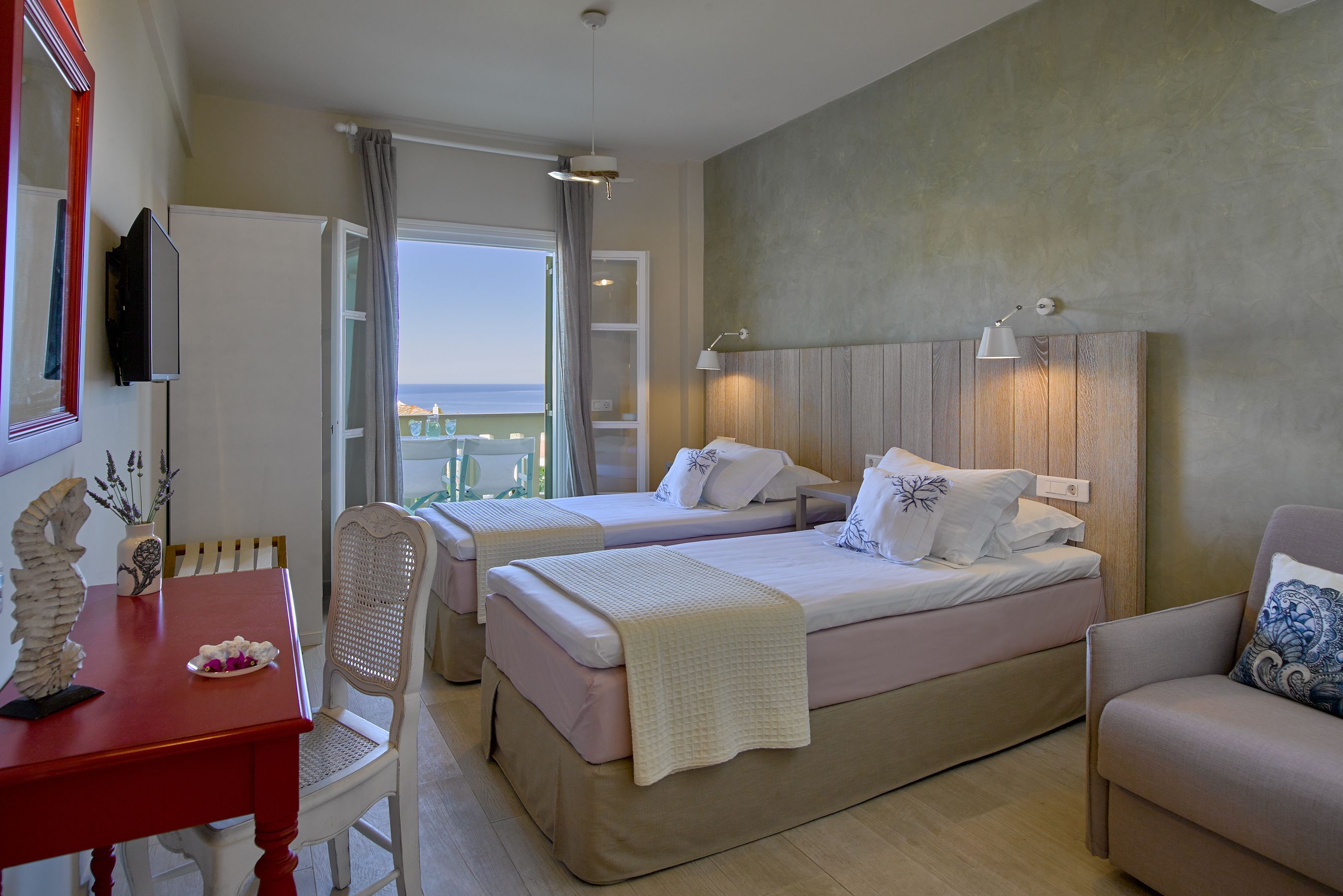Habitación de hotel con dos camas, un escritorio, una silla y vista al mar.