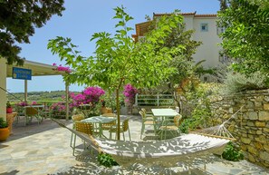 An outdoor patio with tables and chairs, surrounded by potted plants and a hammock. - Konstantina Studios (Alonissos)