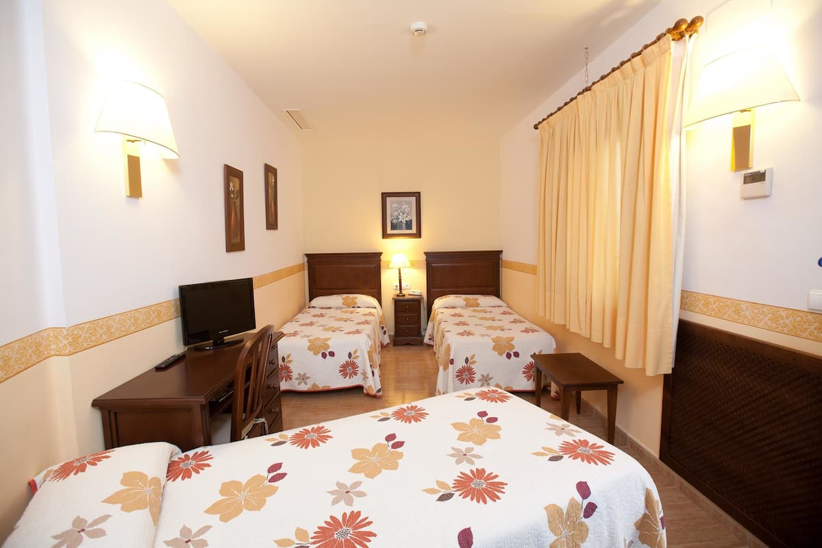 A hotel room with two single beds, a desk with a TV, a bedside table, and a lamp.