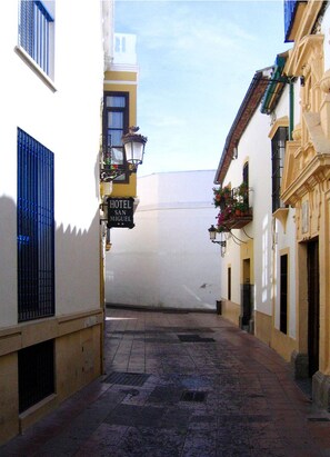 Uma rua estreita com uma placa de hotel, um poste de luz e um edifício com varanda.