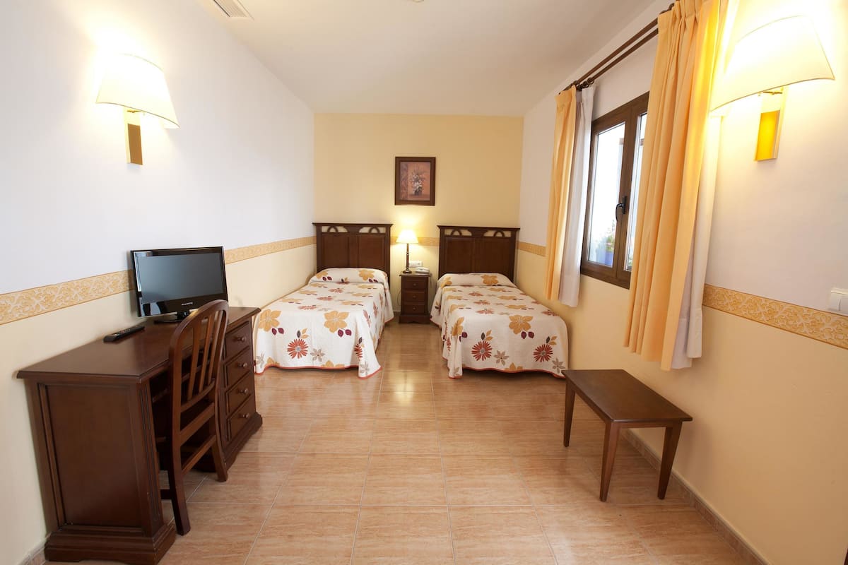 A hotel room with two single beds, a desk with a television, and a small table.