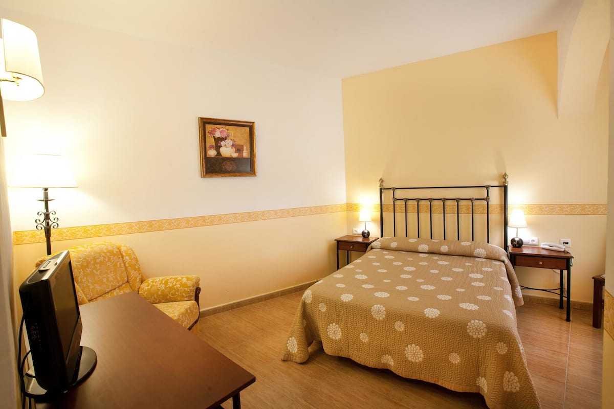 A hotel room with a bed, a desk, a chair, a TV, and a lamp.