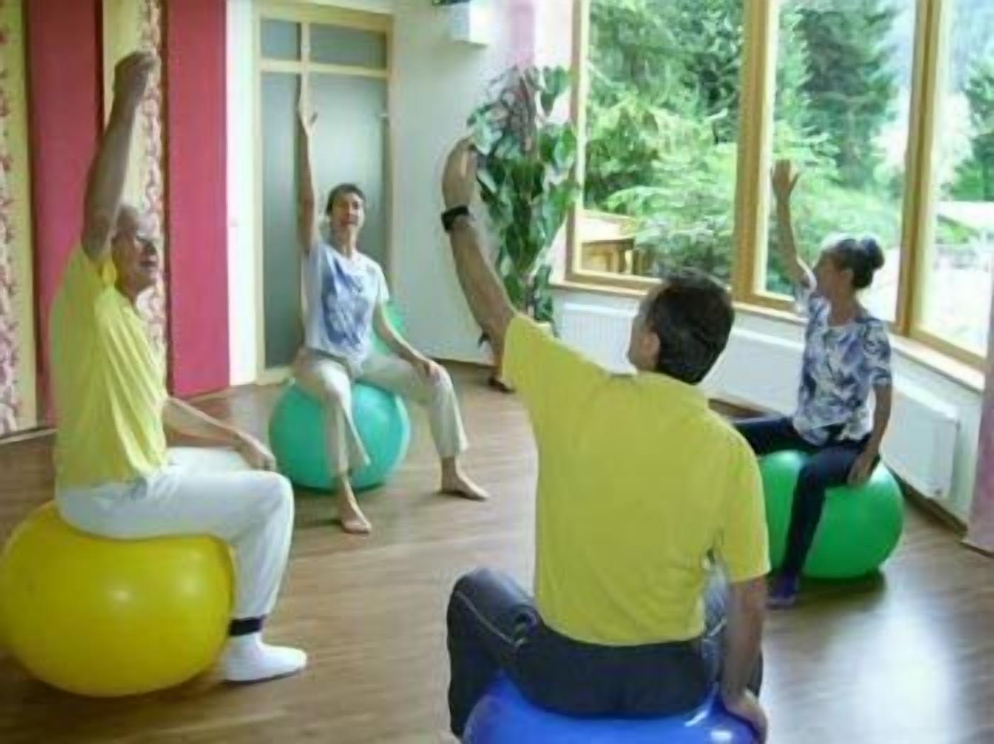 Un grupo de personas ejercitando en grandes pelotas de gimnasia en una habitación con pisos de madera y ventanas amplias.