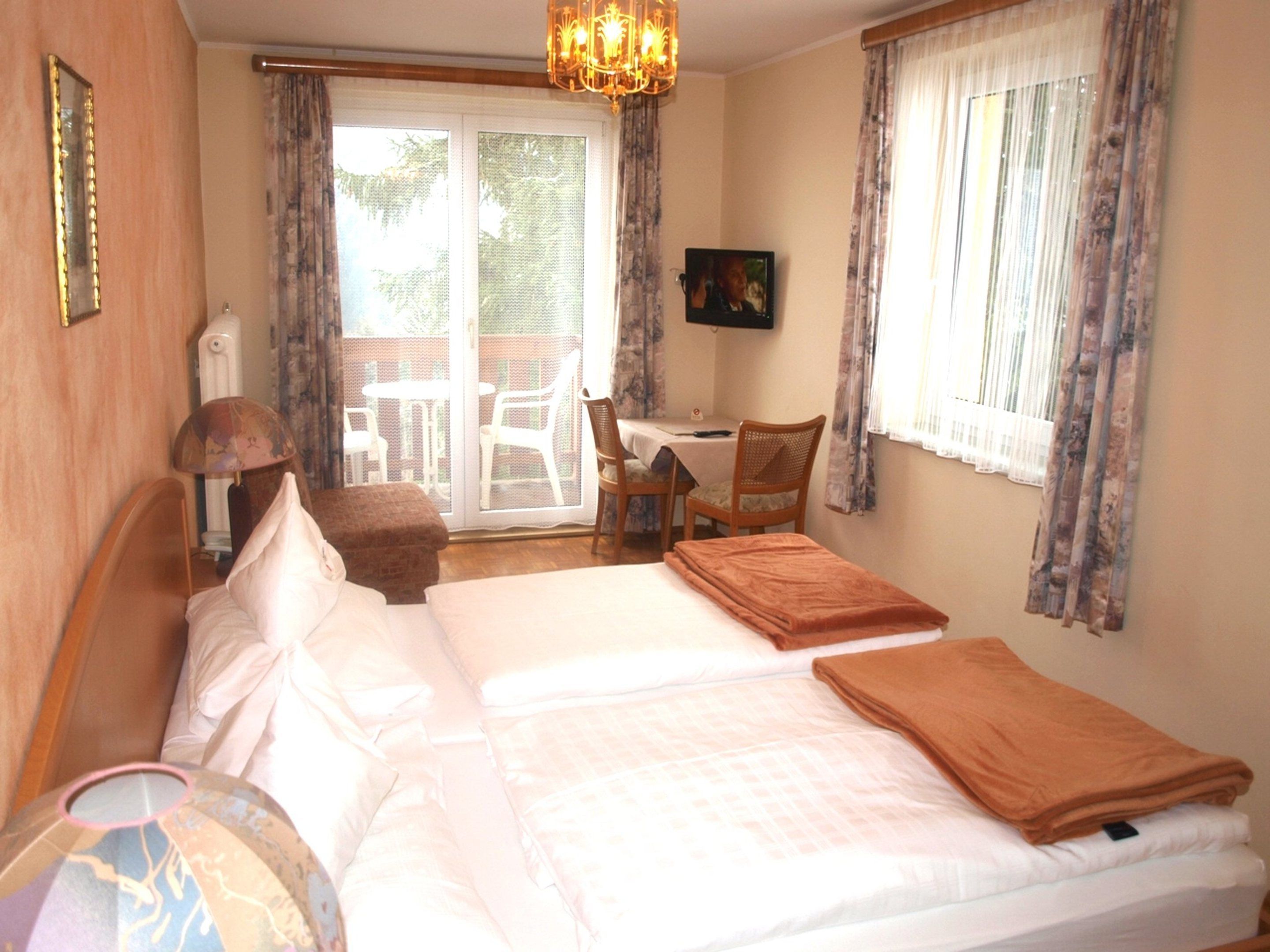 Habitación de hotel con cama, escritorio y silla. Se ve un ventanal con cortinas y vistas al exterior.