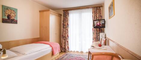 A hotel room with two single beds, a desk with a chair, a TV, and a large window with curtains.