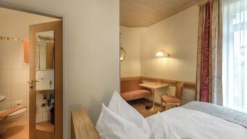 A hotel room with a bed, a bathroom with a sink and mirror, a small table, and a window with curtains.