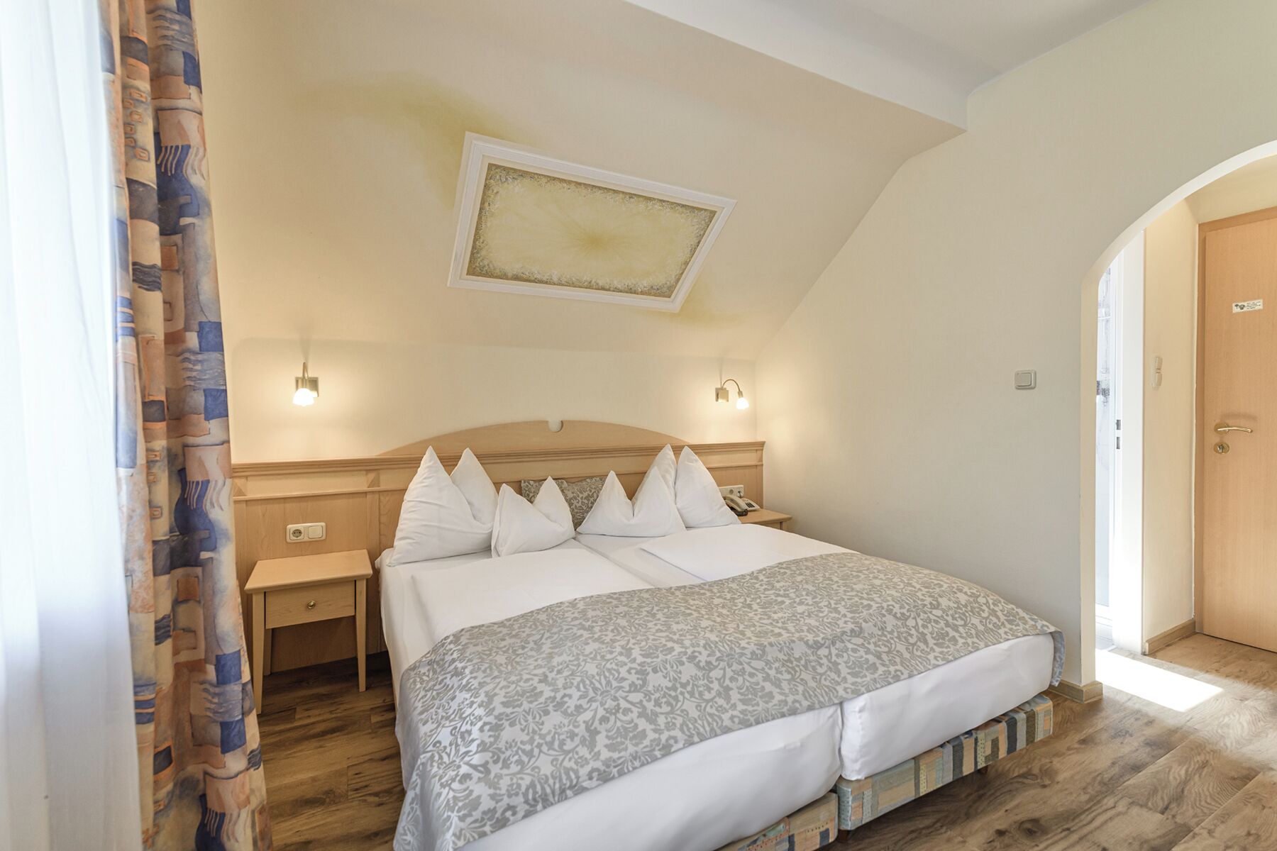 A bedroom with a wooden headboard, a bed with white bedding, a nightstand, and a wall-mounted light fixture.