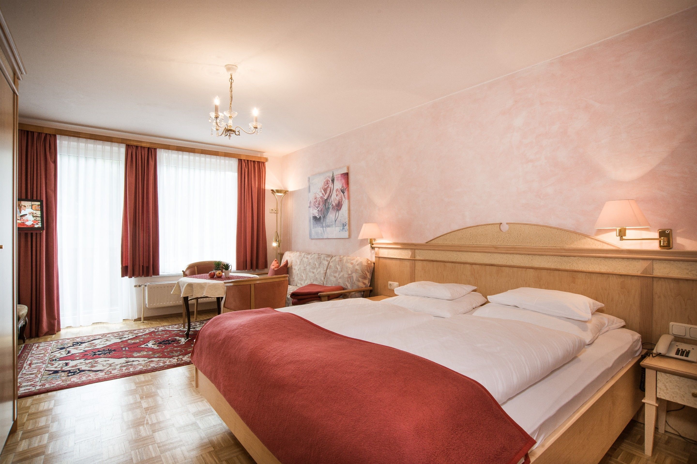 A hotel room with a large bed, a desk with a chair, a small table, a nightstand, and a lamp.