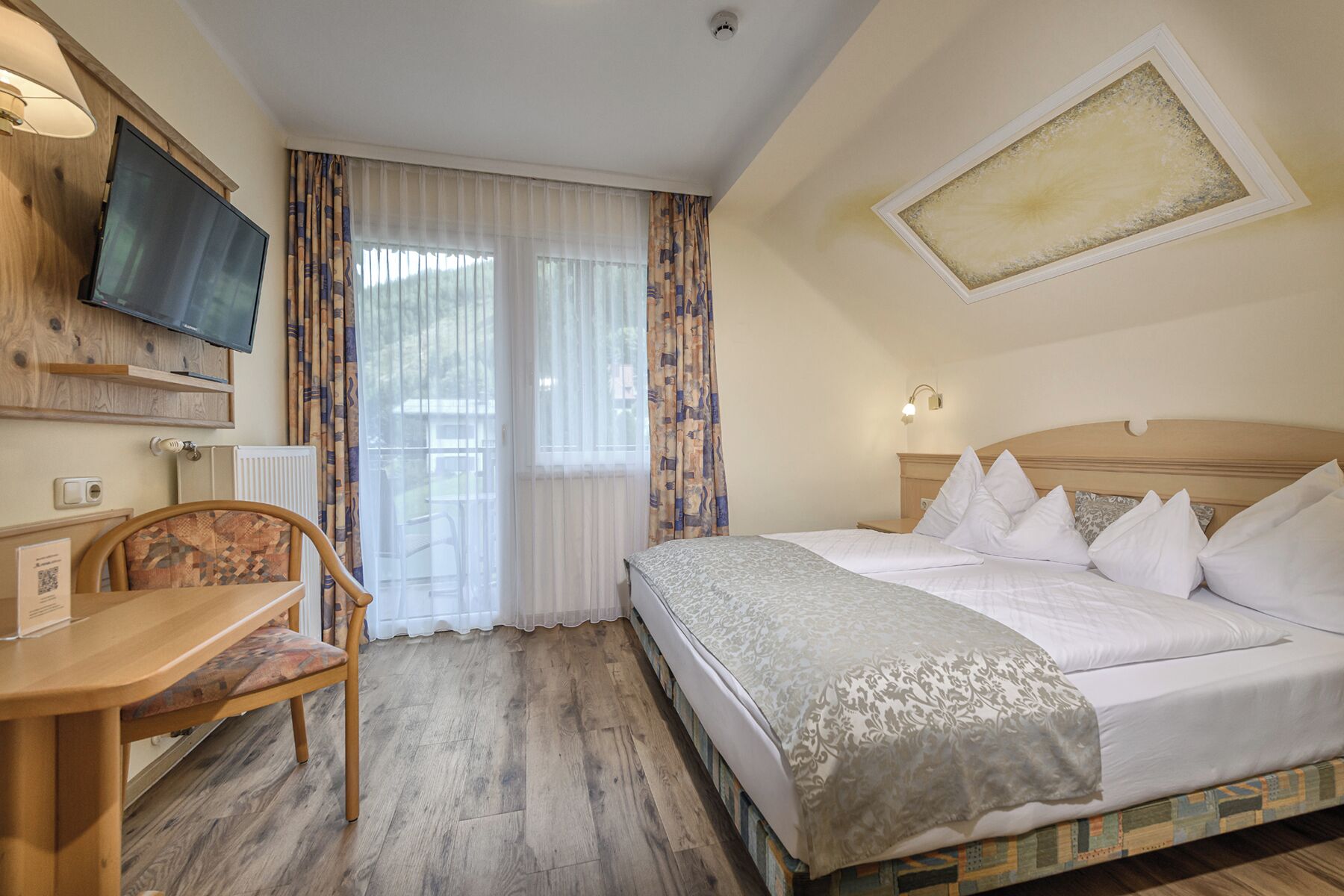 A hotel room with a bed, a desk, a chair, a television, and a window with curtains.