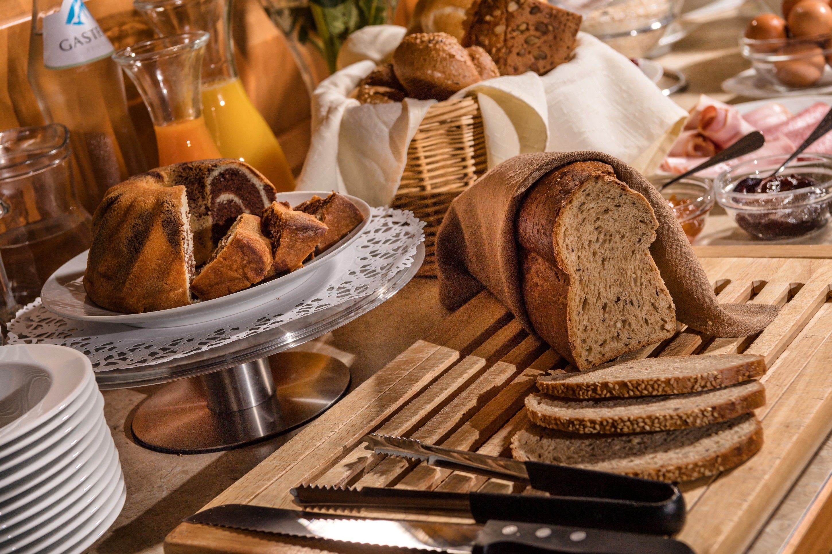 Desayuno con pan, pasteles y condimentos sobre una mesa de madera.