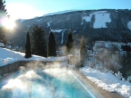 A hot spring surrounded by snow-covered mountains and trees.