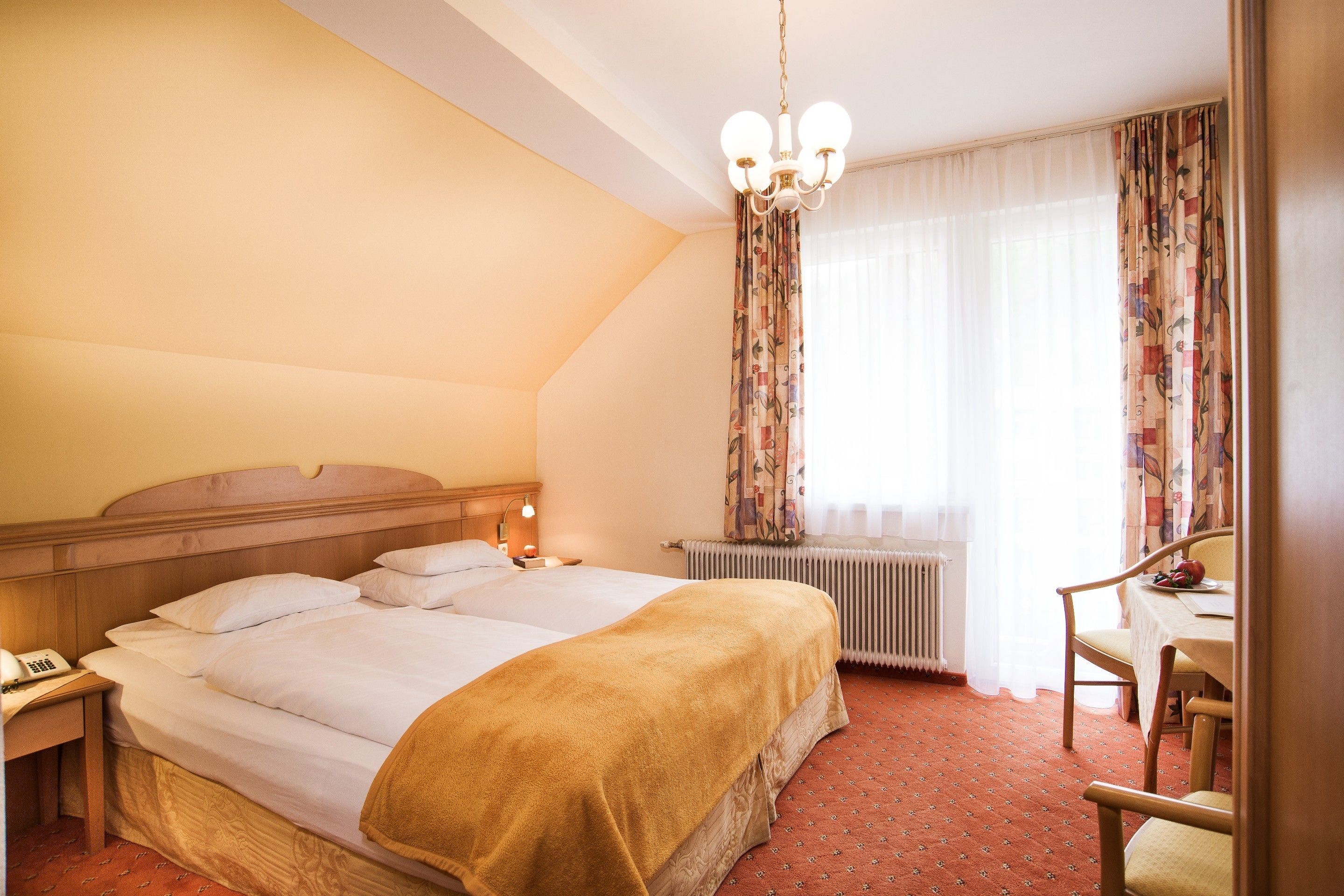 A hotel room with a large bed, a bedside table with a lamp, a chair, and a window with curtains.