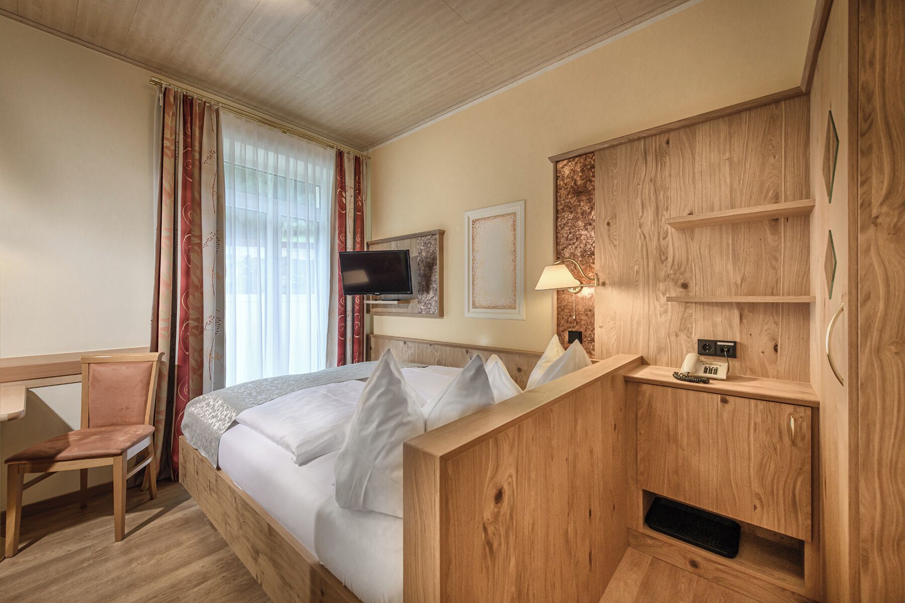 A hotel room with a bed, a desk, a chair, a TV, and a wooden cabinet.