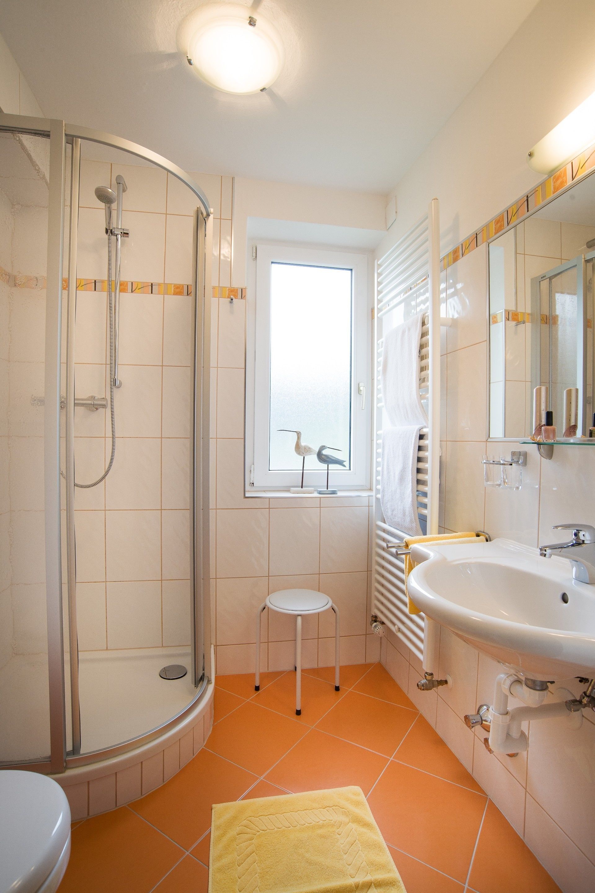 A bathroom with a glass shower enclosure, a white sink, and a window with a view of the sky.