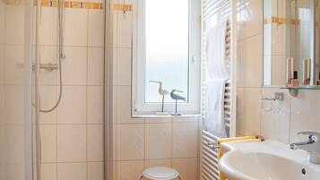 A bathroom with a glass shower enclosure, a white sink, and a window with a view of the sky.