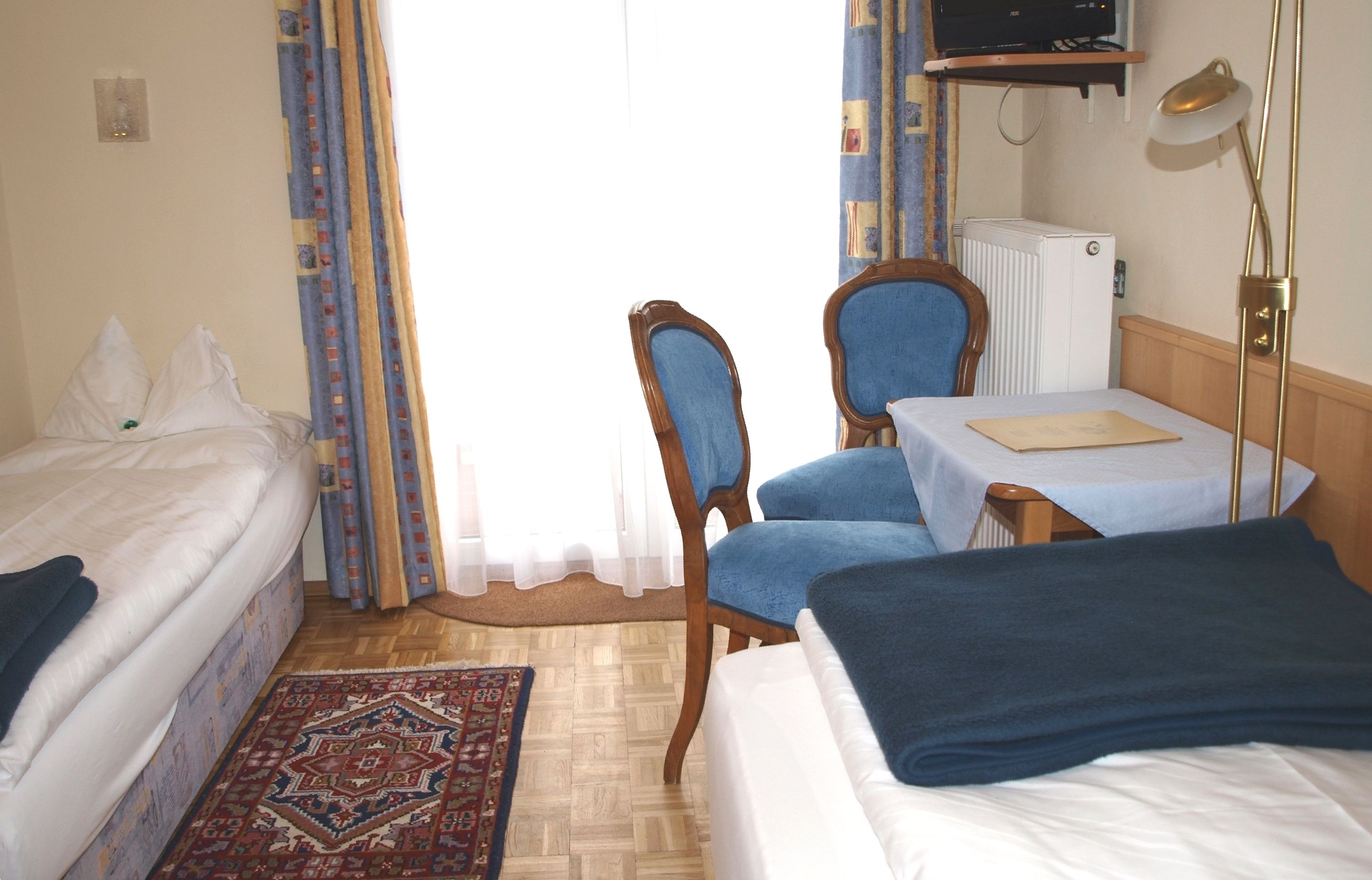 Hotellihuone, jossa on sänky, työpöytä tuolilla, patteri ja televisio hyllyllä.