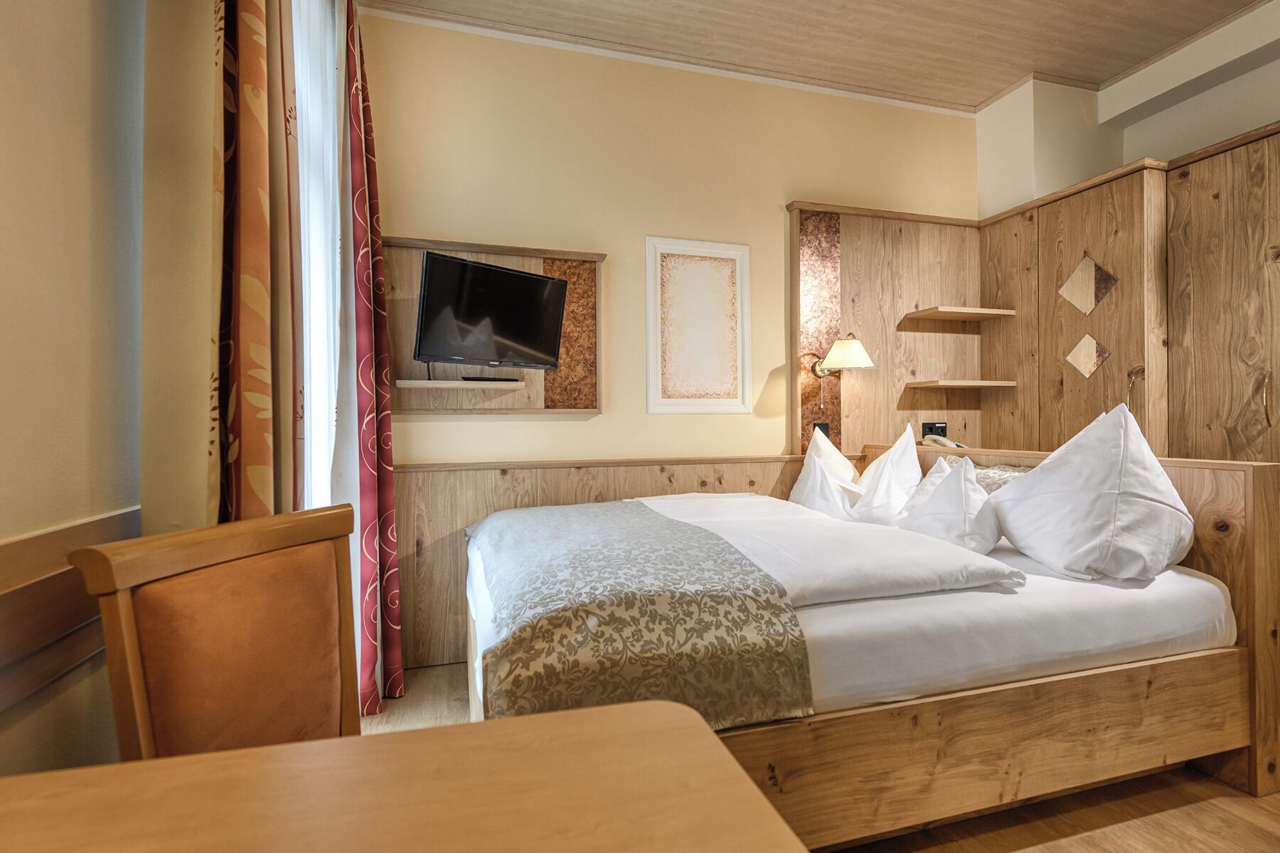 Una habitación de hotel con una cama, televisión, escritorio y armario.