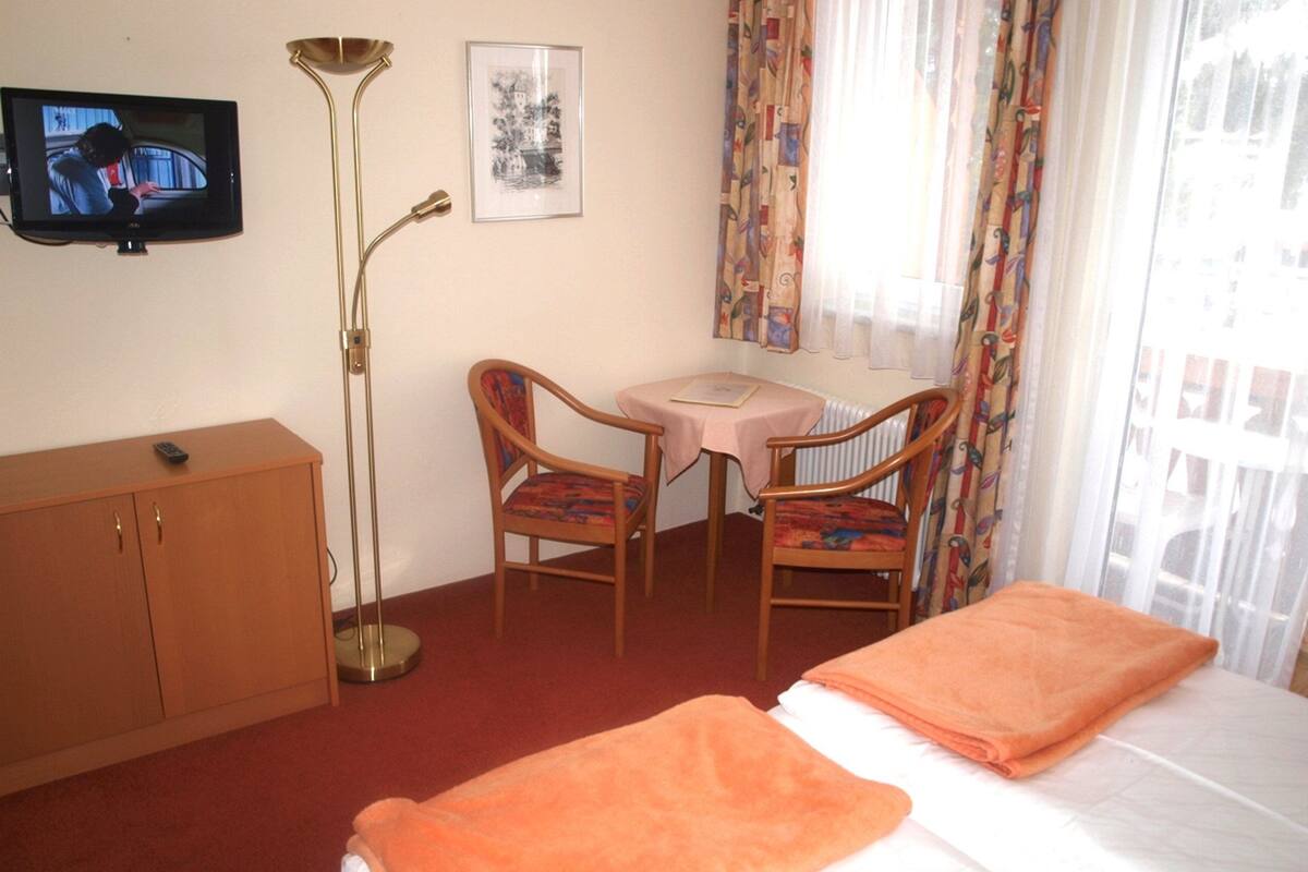 Ein Hotelzimmer mit einem Bett, zwei Stühlen, einem Schreibtisch, einem Fernseher und einer Stehlampe.