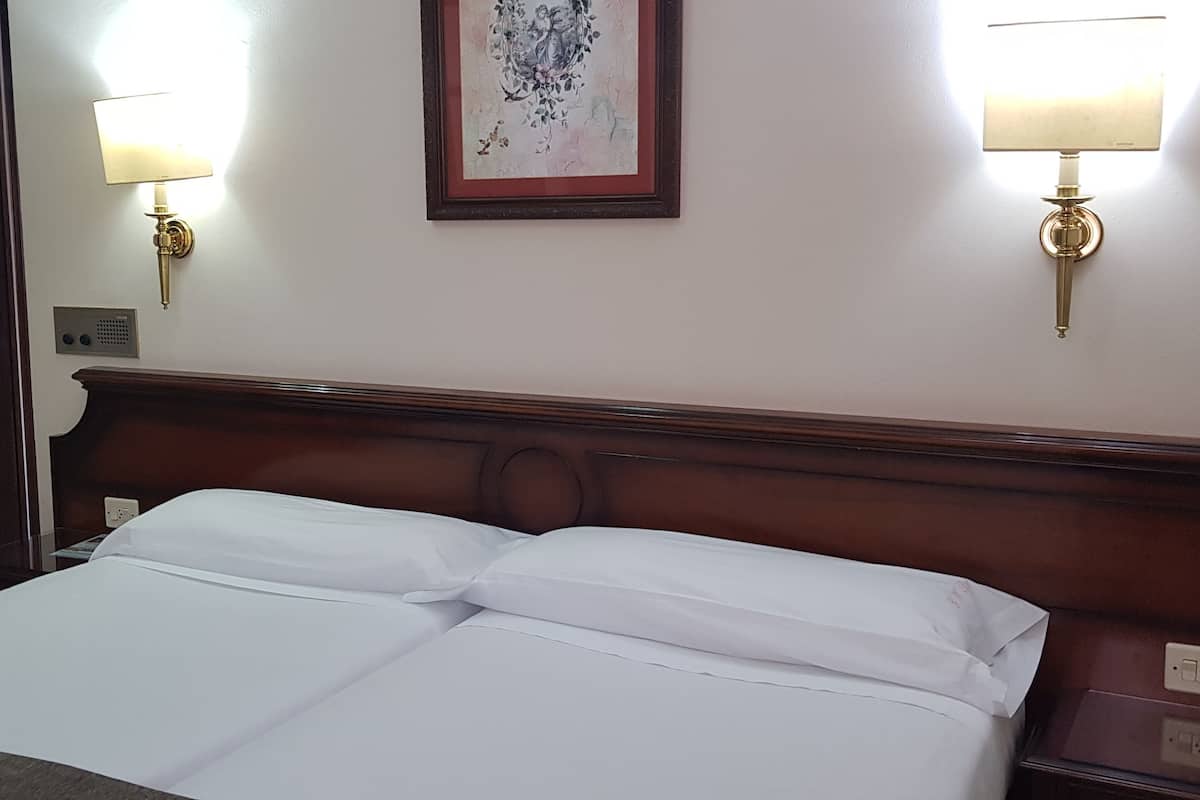 Quarto de hotel com uma cama bem arrumada, duas luminárias fixadas na parede, uma obra de arte emoldurada e uma porta.