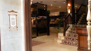 A hotel lobby with a marble floor, a staircase with floral carpet, and a sign with 'Llanes' and 'H. Pannesso' visible. - Gran Hotel Paraiso (Llanes)
