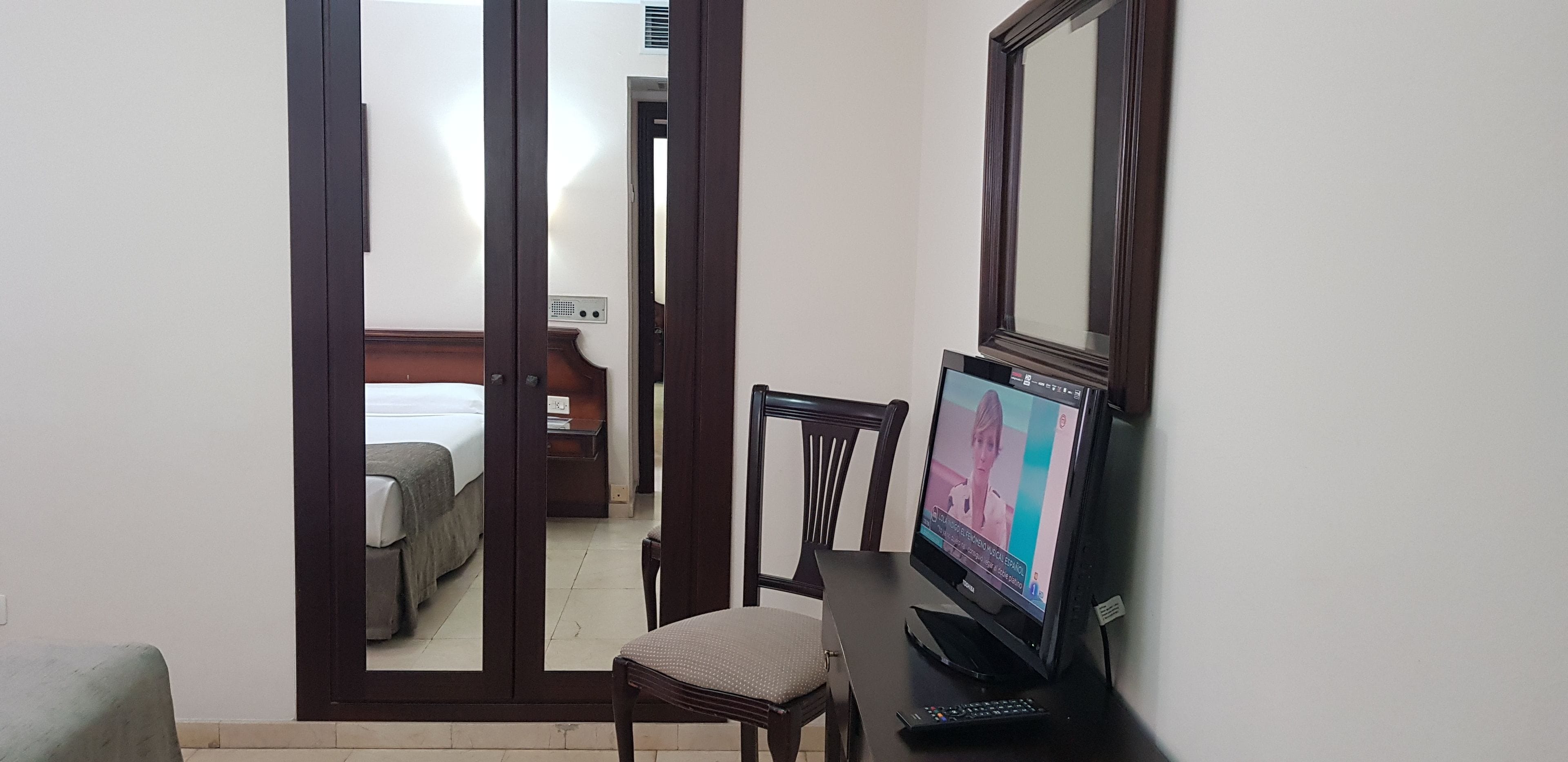 A hotel room with a bed, a desk with a computer, and a chair.
