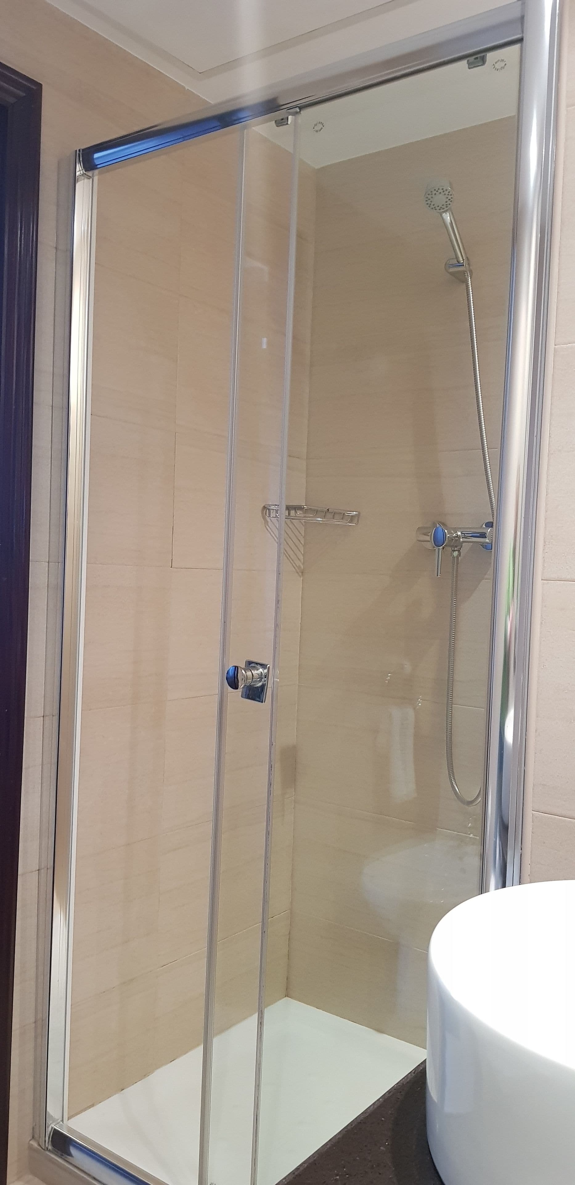 Um chuveiro com box de vidro, um chuveiro manual e uma torneira fixada na parede.