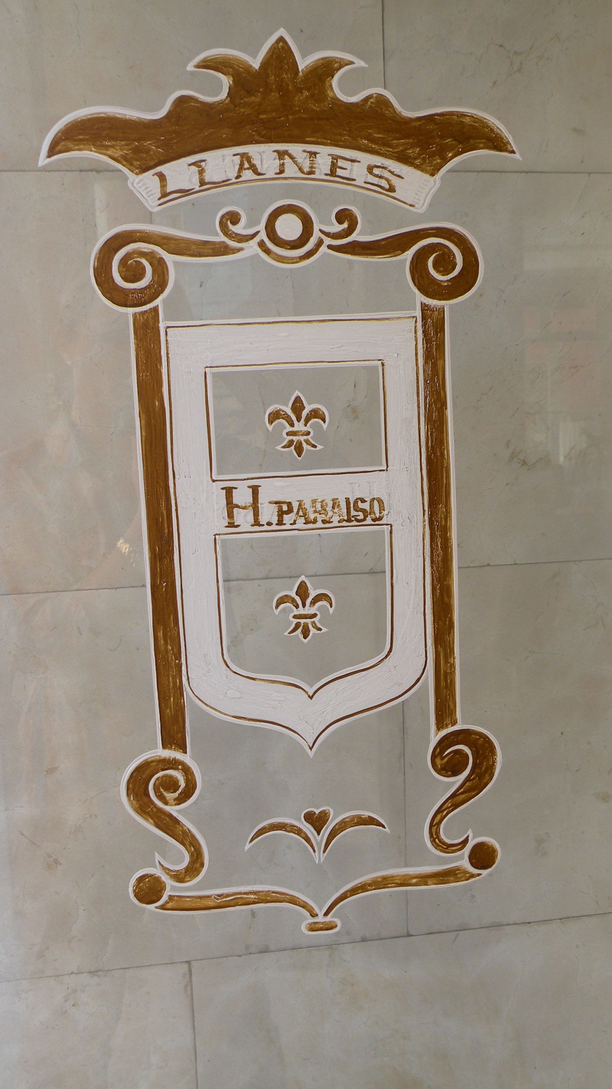 Une enseigne décorative portant les noms « Llanes » et « H. Paraiso » dans une police stylisée, entourée d’éléments dorés et blancs travaillés.