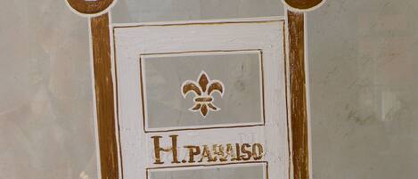 A decorative sign with the name "Llanes" and "H. Paraiso" in a stylized font, surrounded by ornate gold and white elements.