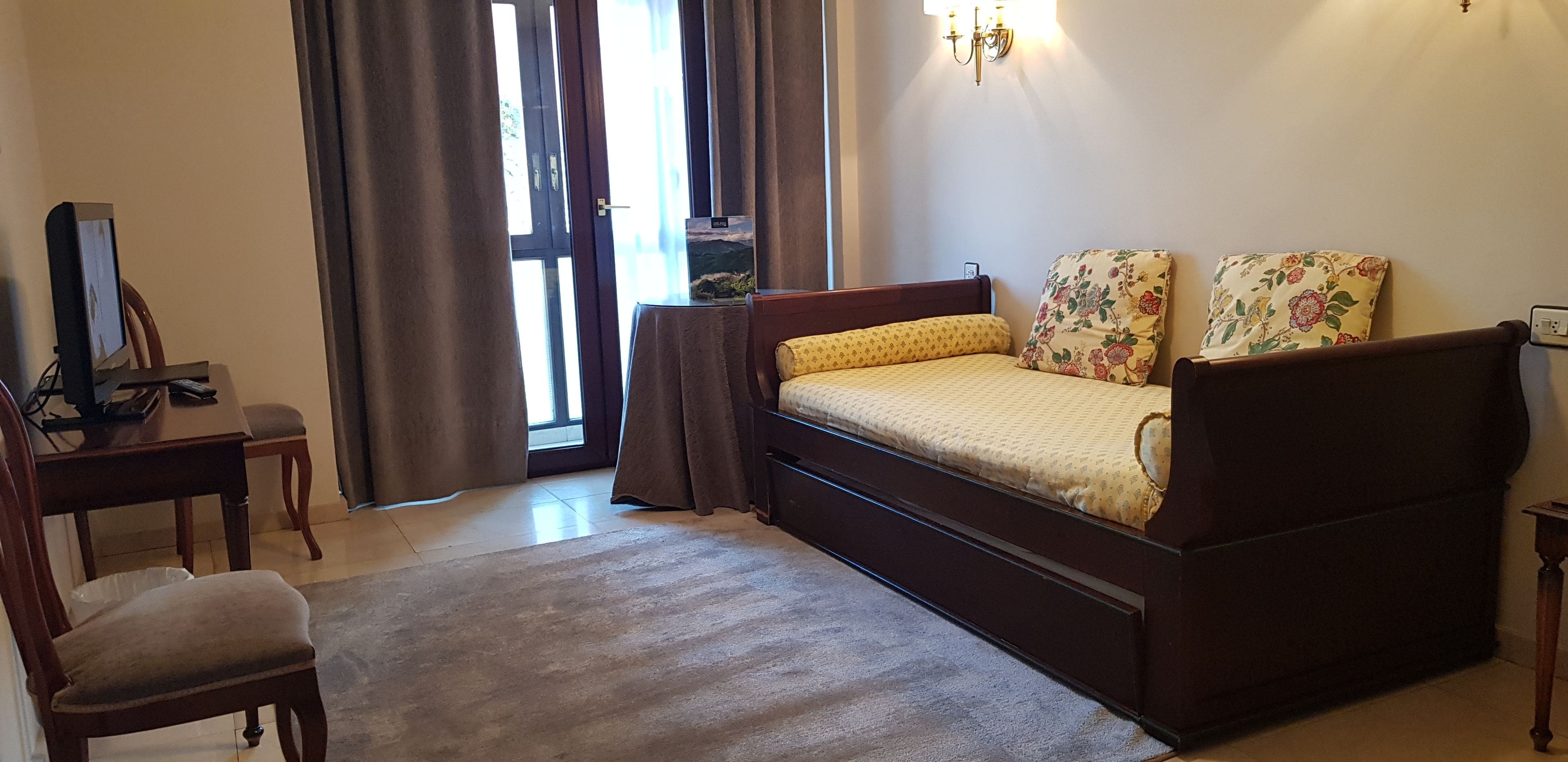 Un dormitorio con cama, escritorio, silla, lámpara y ventana con cortinas.
