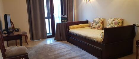 Un dormitorio con cama, escritorio, silla, lámpara y ventana con cortinas.