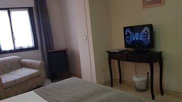 Una habitación de hotel con cama, sofá, televisor sobre una mesa de madera y ventana con cortinas.