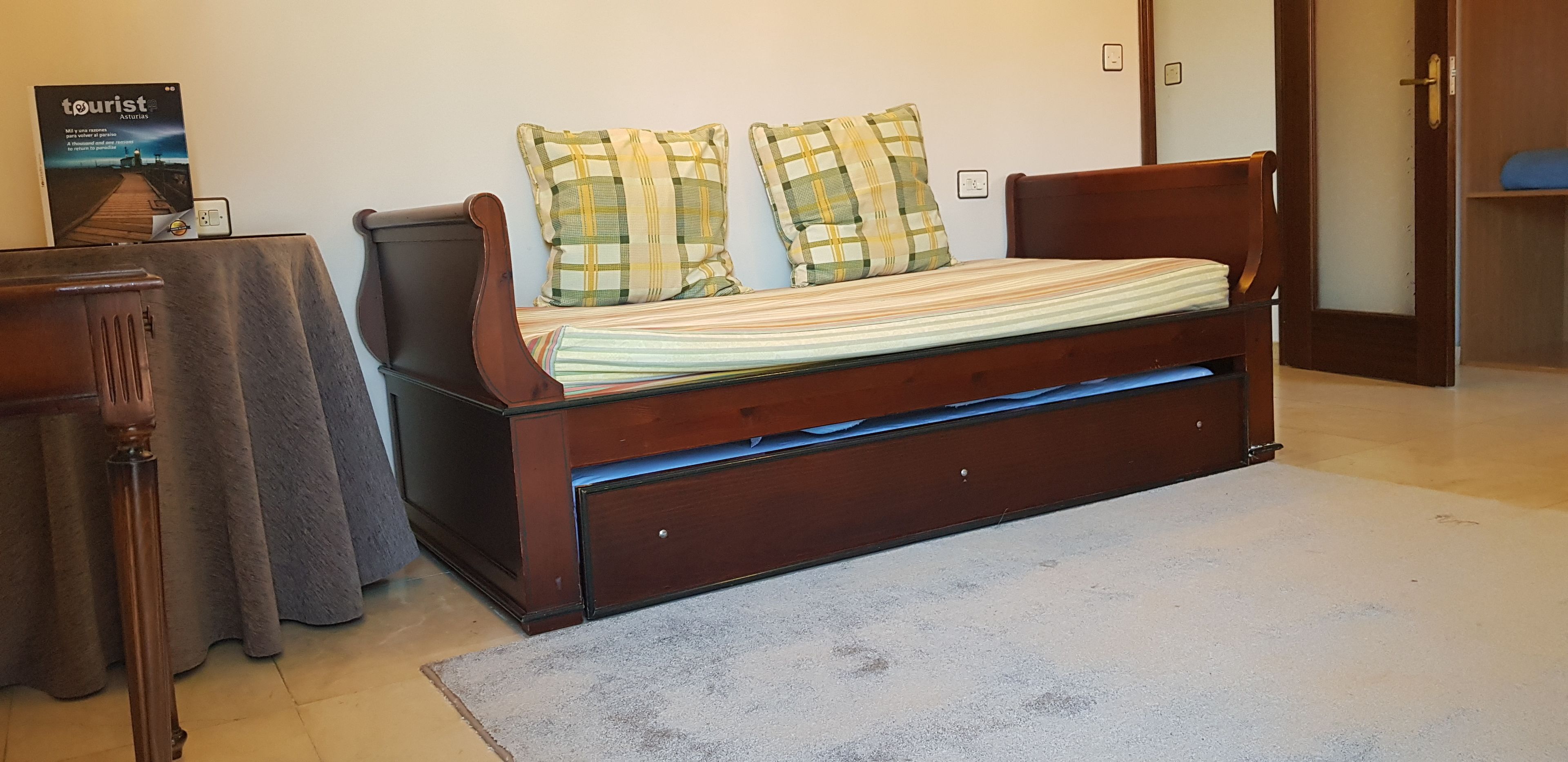 A wooden bed with a striped mattress and two plaid pillows, a wooden nightstand, and a poster on the wall.