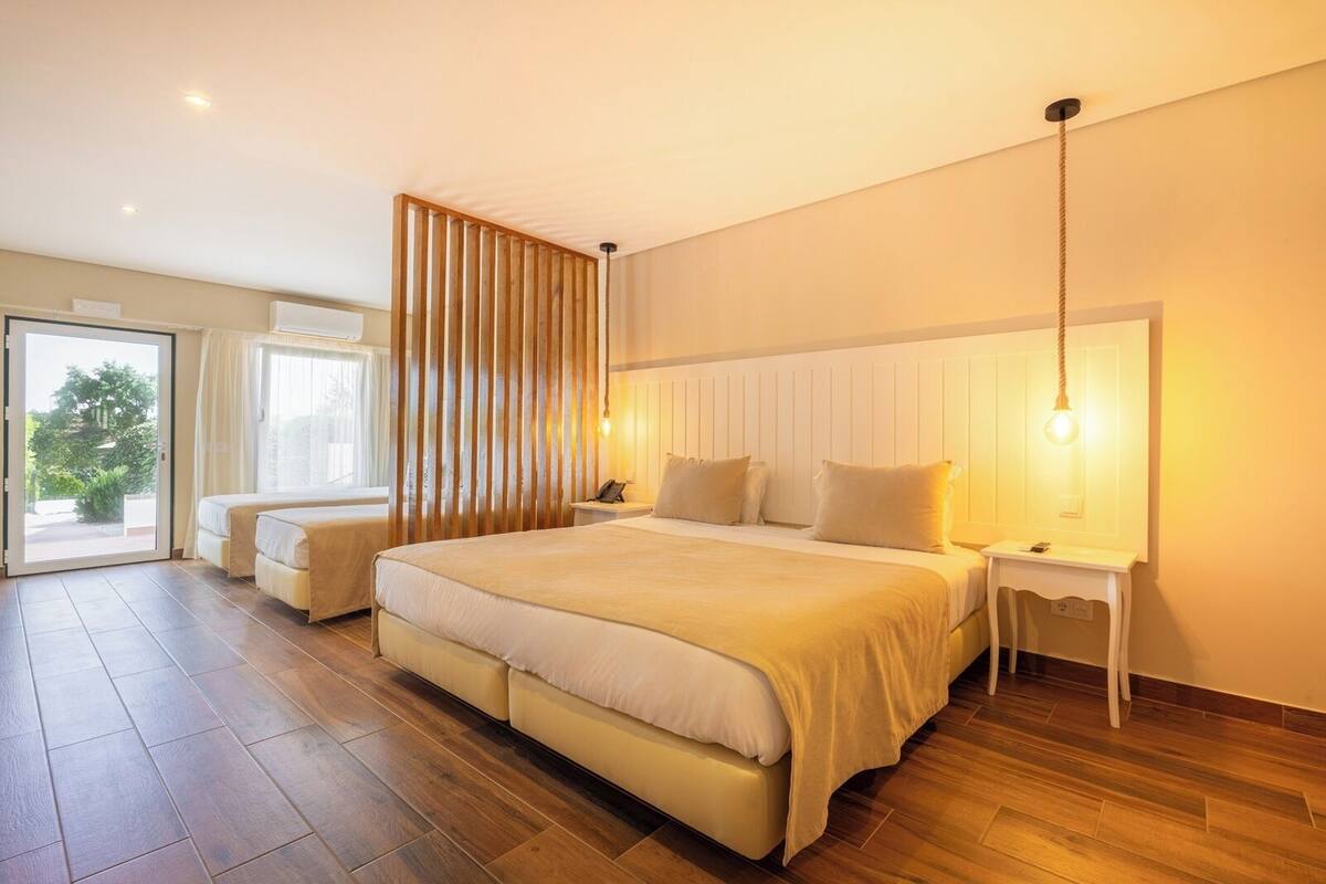 A spacious bedroom with a large bed, bedside tables, a wooden slat partition, and a view through a sliding door.