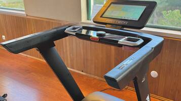 A stationary bike with a digital screen, a tray with a water bottle, and a wall-mounted picture.
