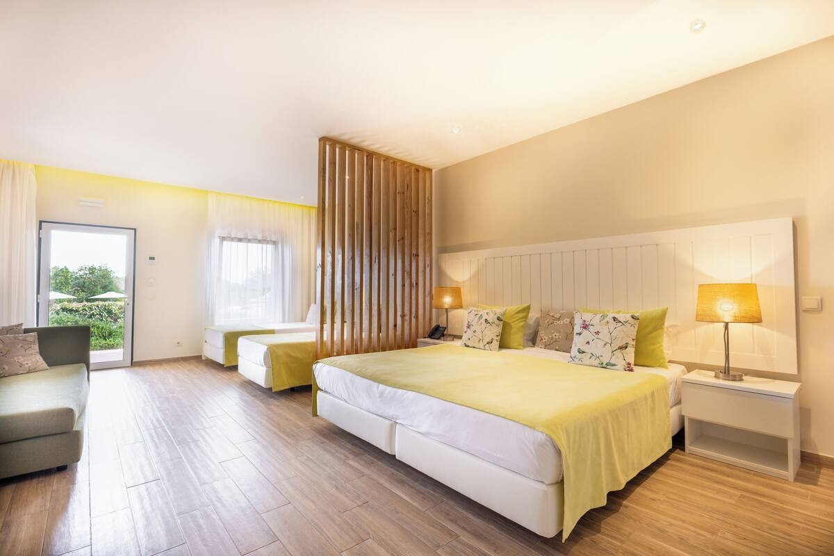 A spacious bedroom with a large bed, two bedside tables with lamps, a sofa, and a sliding door leading to a balcony.
