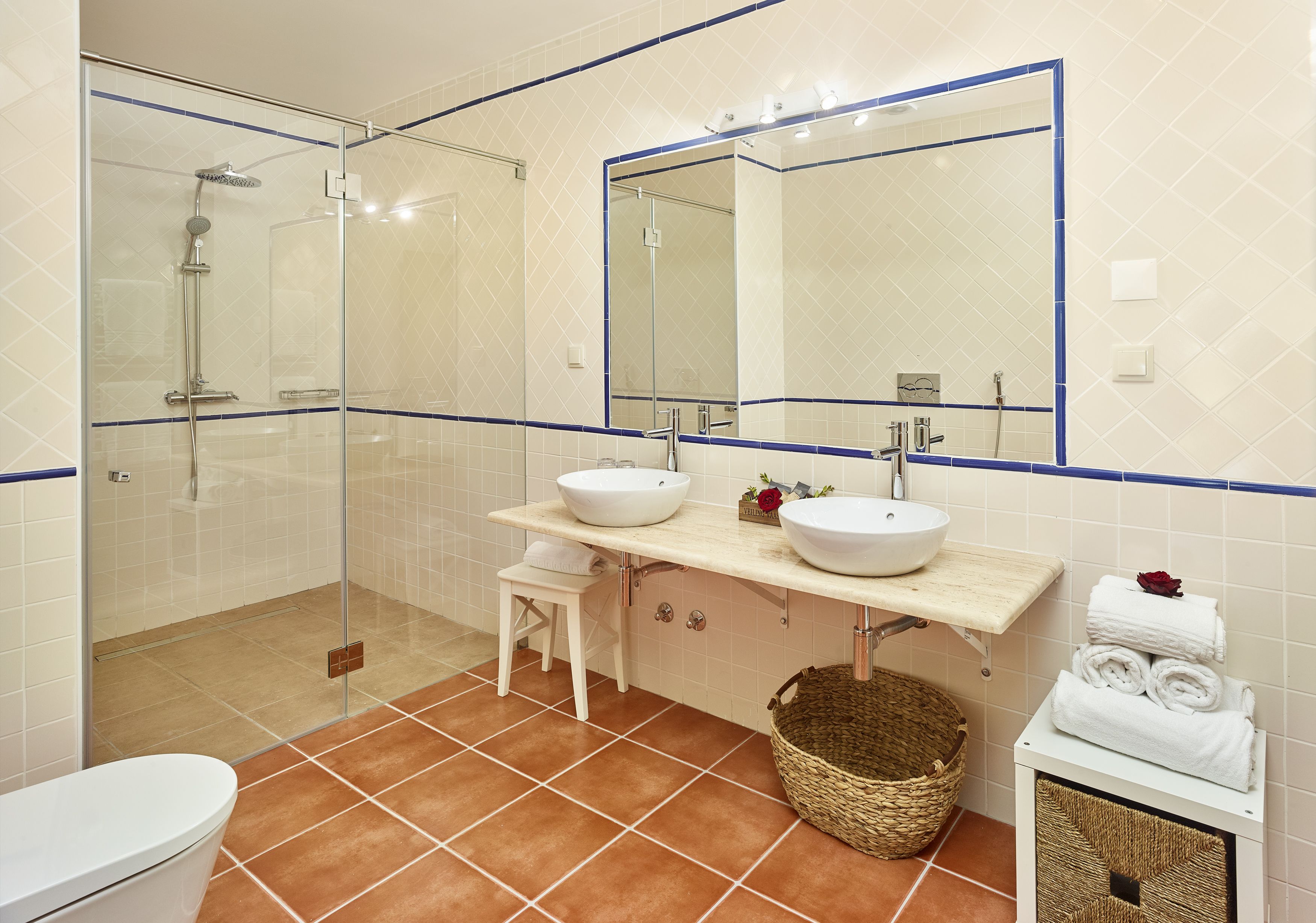 A bathroom with a glass-enclosed shower, two sinks, a large mirror, and a white toilet.