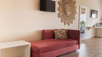 Una sala moderna con un sofá rojo, una consola blanca, un gran tapiz decorativo y un televisor de pantalla plana montado en la pared.
