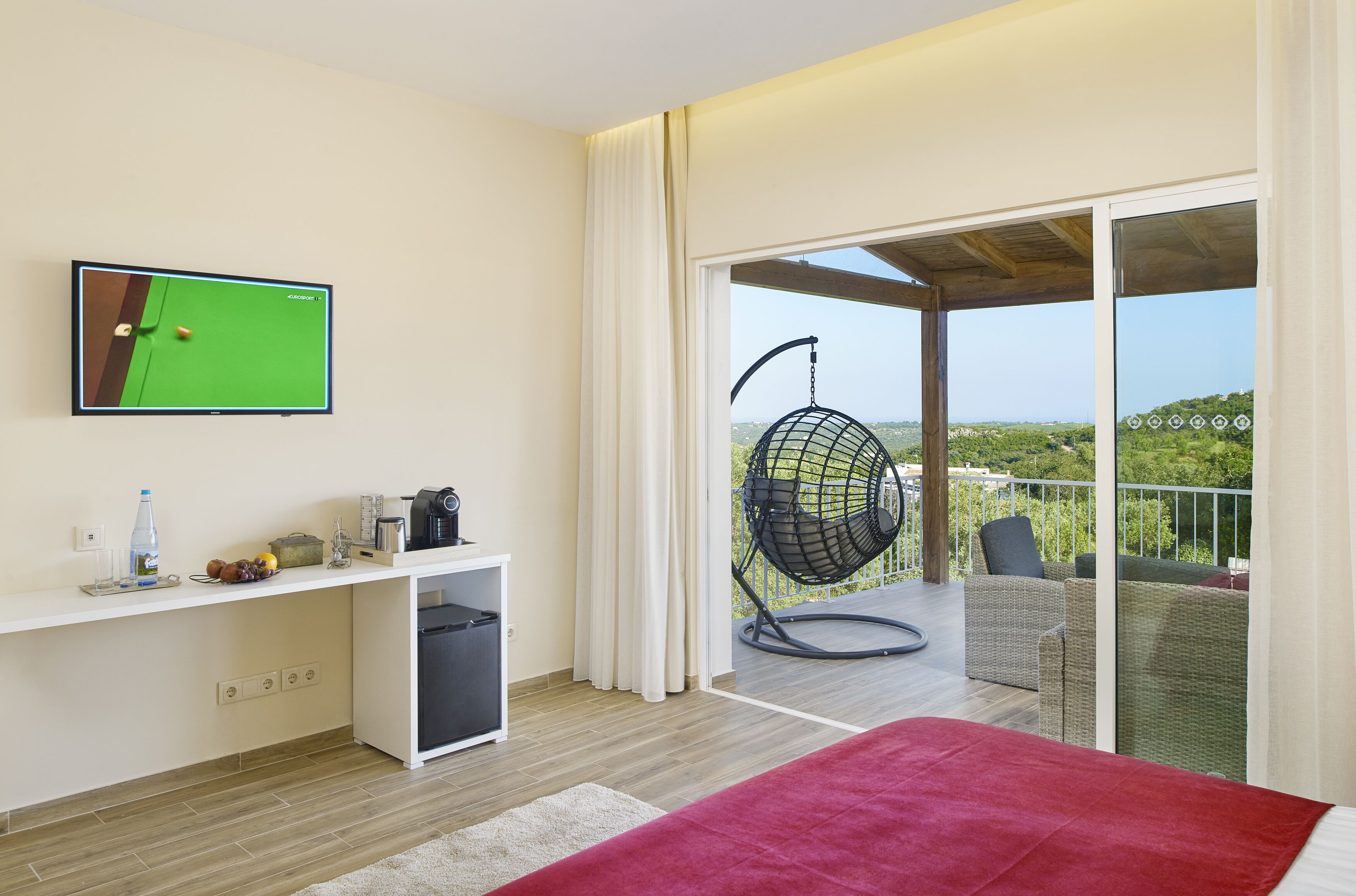 A room with a bed, a TV, a balcony with a hanging chair, and a view of the outdoors.