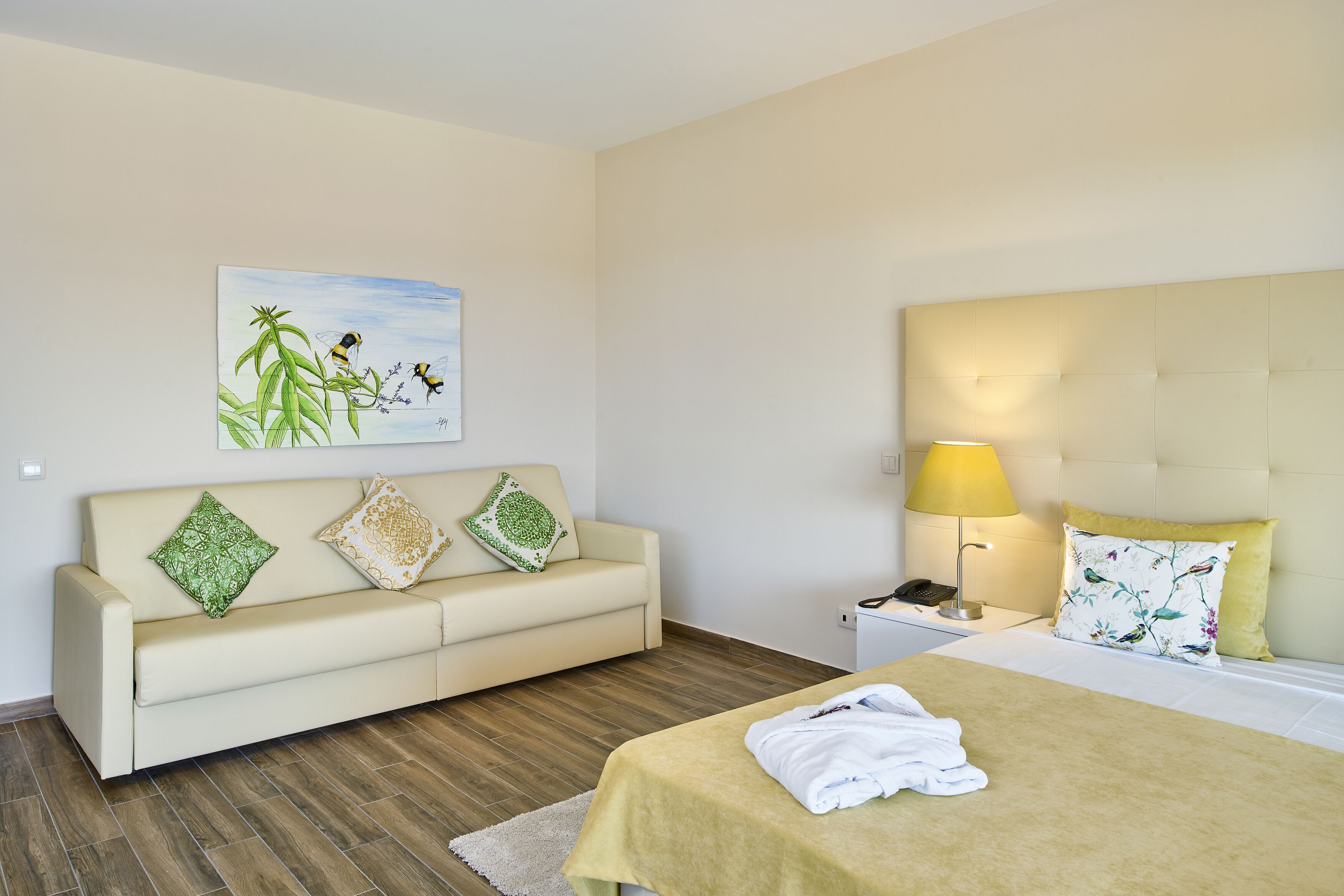 Een hotelkamer met een bed, een slaapbank, een nachtkastje, een lamp en een schilderij aan de muur.
