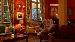 Una sala de estar acogedora con un sofá verde, sillones estampados, una mesa de centro de madera y un piano al fondo.