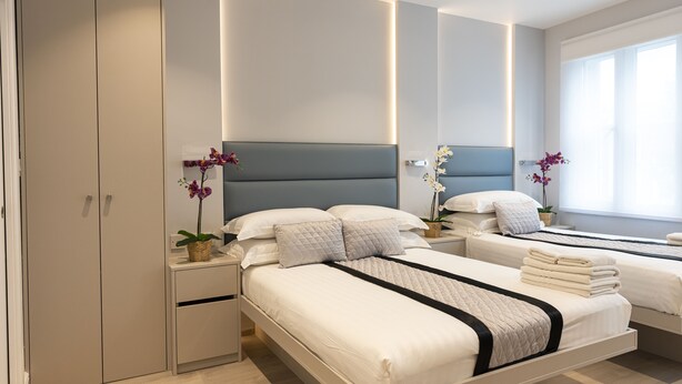 A modern bedroom with two beds, a wardrobe, and a large window.
