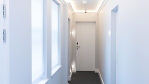 A narrow, well-lit hallway with white walls and a dark carpet.