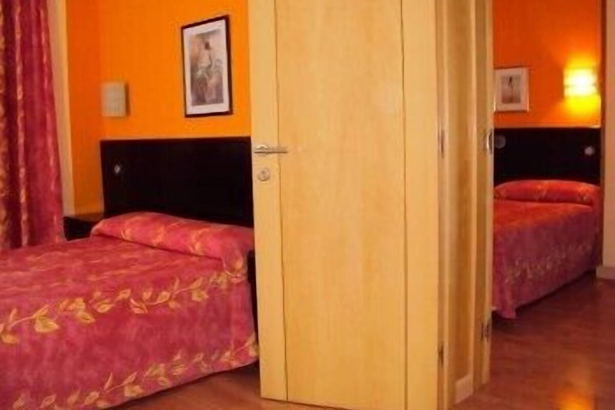 Habitación de hotel con dos camas, paredes anaranjadas y una puerta de madera.