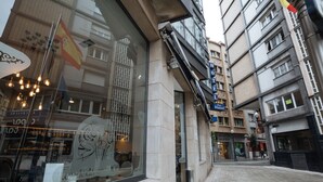 A hotel with a large window displaying a vintage poster, a sign for 'HOTEL Don Manuel', and a tiled sidewalk. - Hotel Don Manuel (Gijon)