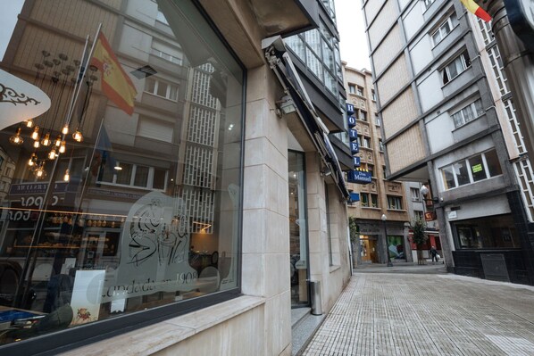 A hotel with a large window displaying a vintage poster, a sign for 'HOTEL Don Manuel', and a tiled sidewalk.